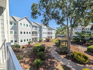 A multi-story residential building with a landscaped courtyard, a pergola, and a clear sky.