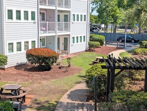 A multi-story building with balconies, a patio area with a grill, and a well-maintained lawn.