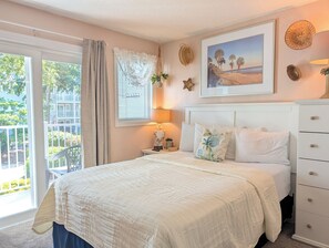 Un dormitorio con cama, mesita de noche, lámpara, ventana con cortinas e imagen enmarcada en la pared.