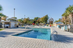 Zona de piscina con puesto de socorrista, sillas de descanso y un pequeño edificio con un cartel.