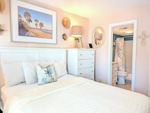 A bedroom with a bed, a dresser, a mirror, and a bathroom visible through an open door.