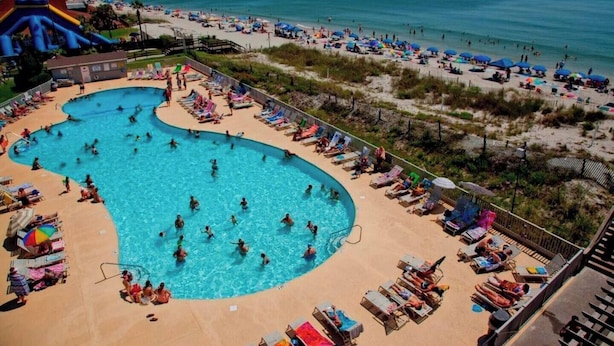 A large swimming pool with multiple lanes, surrounded by beach chairs and umbrellas.