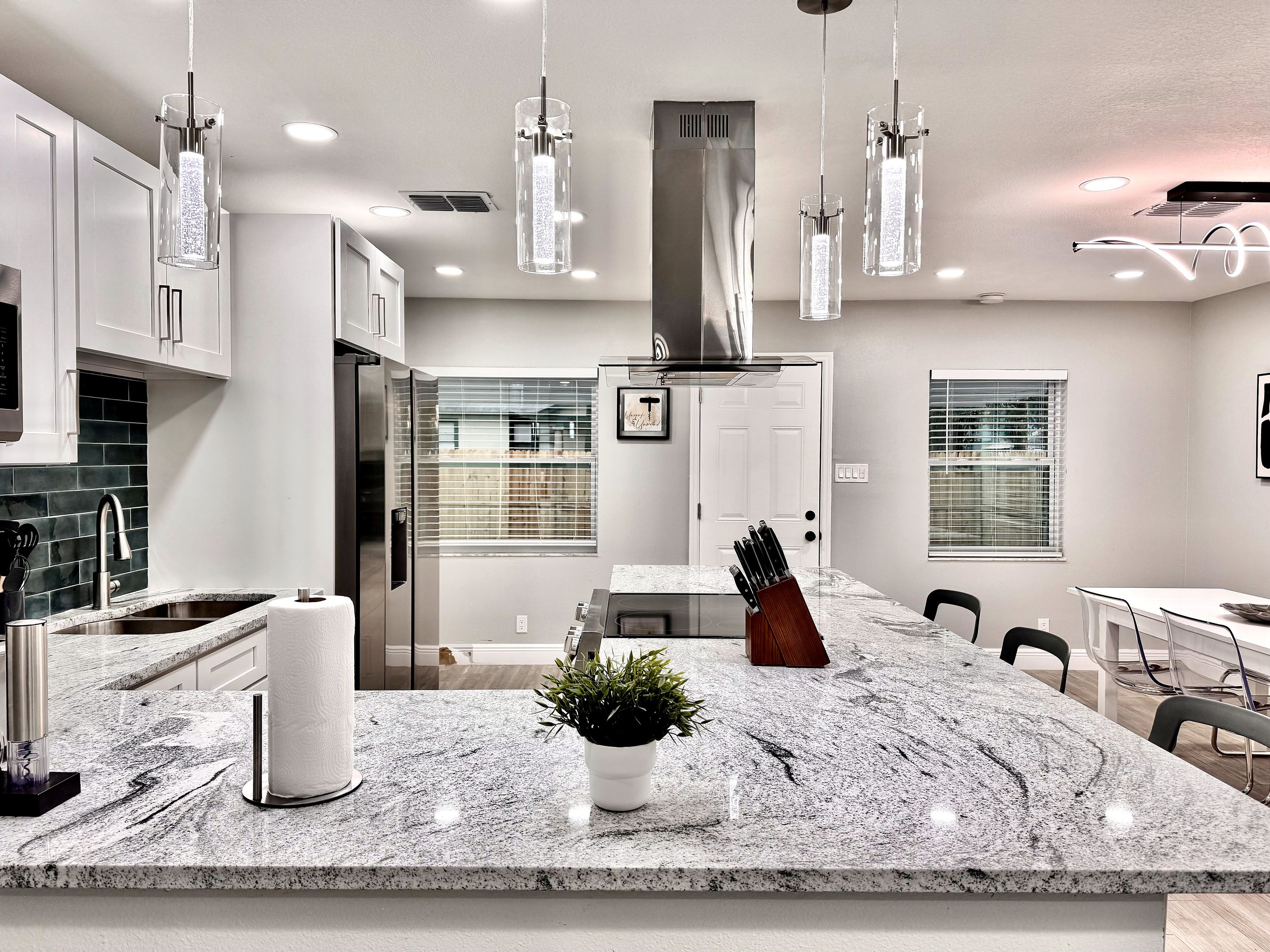 A modern kitchen with granite countertops, stainless steel appliances, pendant lighting, and a central island with a knife block and potted plant.