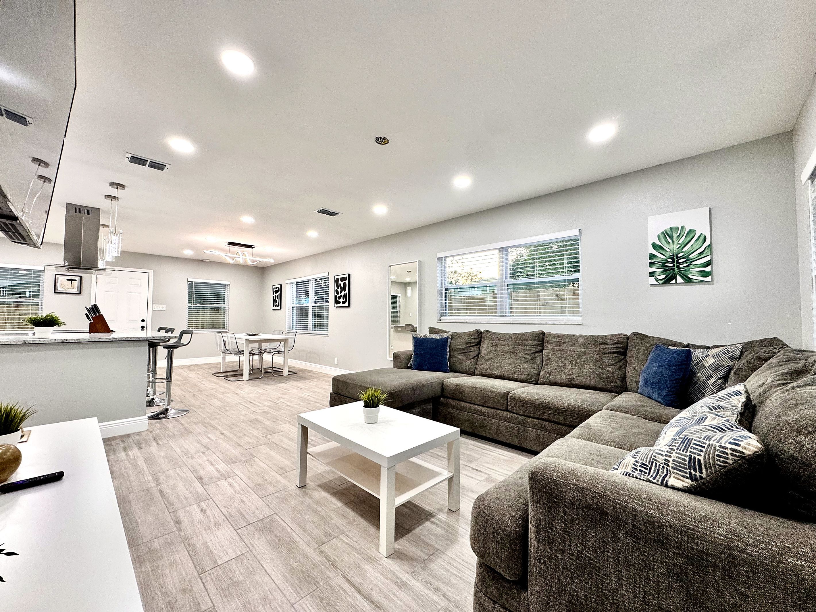 A modern living room with a sectional sofa, a dining area with a table and chairs, and a kitchen area with a countertop and appliances.