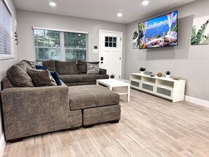 Un salon moderne avec un canapé d’angle, une table basse et une console blanche agrémentée d’objets décoratifs.