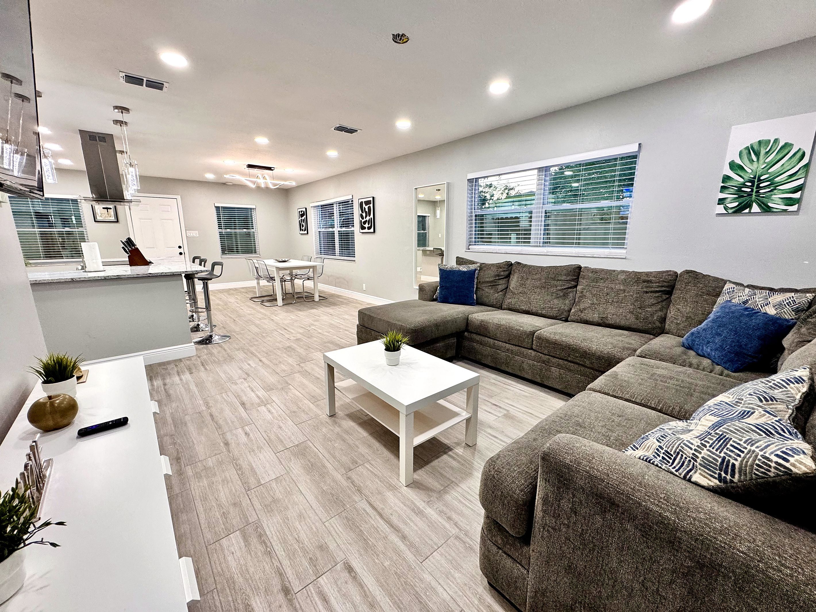 Un salon moderne avec un canapé d’angle, une table basse et un coin repas comprenant une table et des chaises blanches.