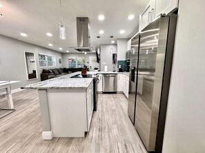 Une cuisine moderne dotée d’un îlot central, d’appareils électroménagers en acier inoxydable et d’un coin repas avec une table et des chaises blanches.