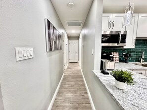 Un couloir avec un interrupteur, une porte et un coin cuisine équipé de placards et d’un four à micro-ondes.
