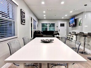Un salon moderne avec une table à manger blanche, un canapé et un téléviseur fixé au mur.