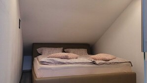 Une chambre avec un plafond en pente, un lit avec une literie à motifs et un éclairage encastré.