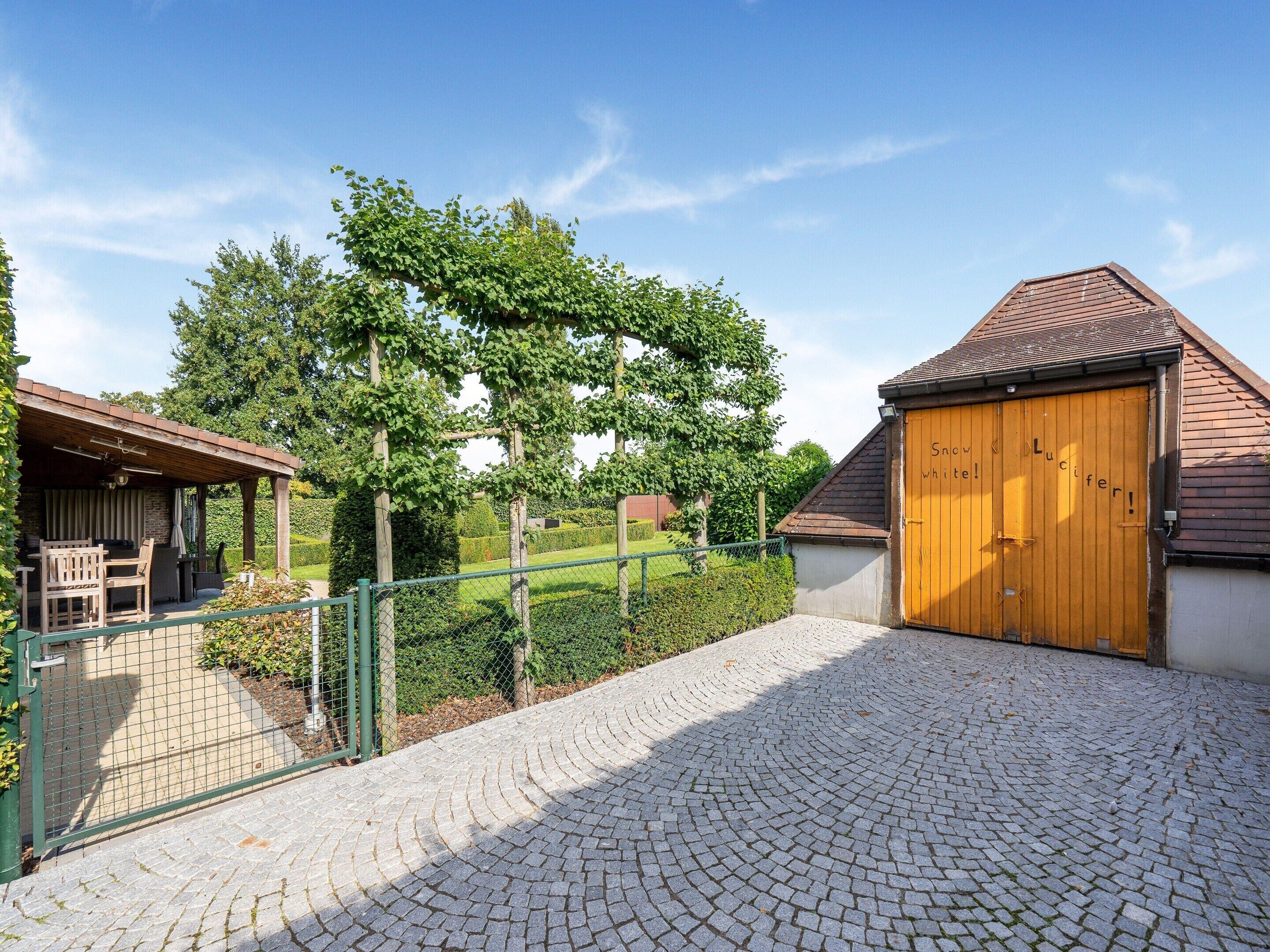 A cobblestone driveway leading to a wooden garage door with the words "Snoo, White, Lucifer!" written on it.