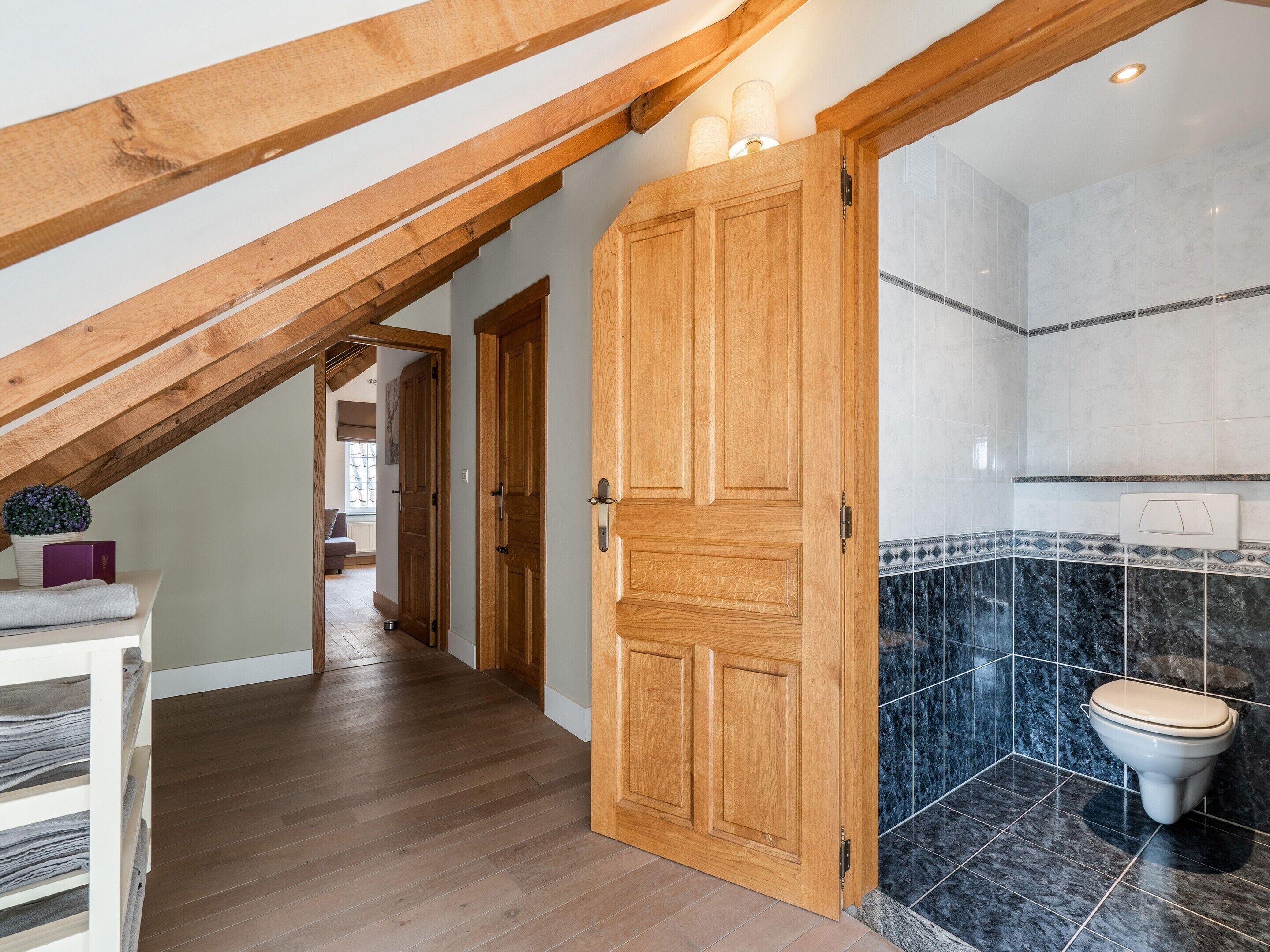 A wooden door leading to a bathroom with a toilet and tiled walls.