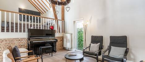 Una sala de estar acogedora con un piano, sillones de mimbre, una mesa redonda y una escalera con vigas de madera.