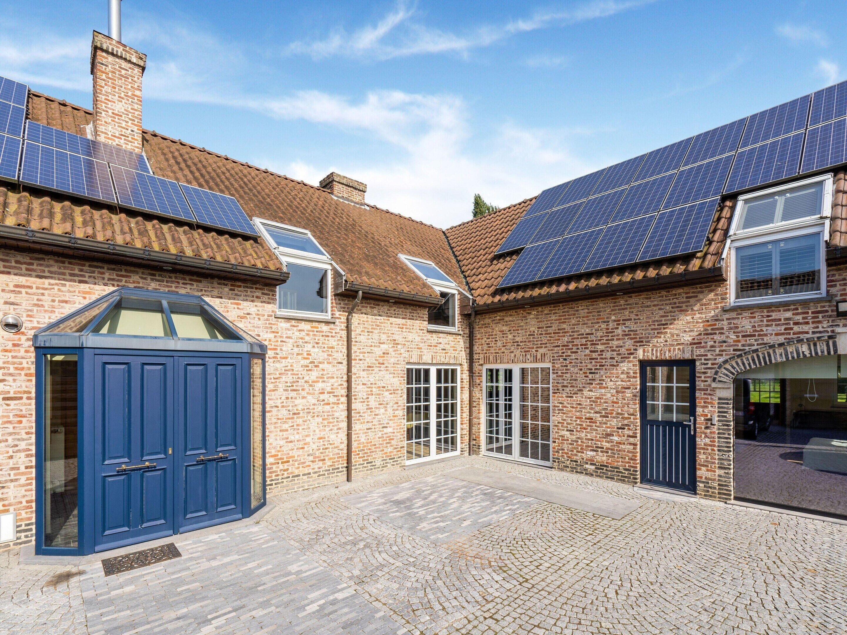 Un patio con un edificio de ladrillo, paneles solares y una puerta azul.