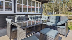 An outdoor patio with wicker furniture, including a sofa and a table with cushions.