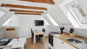 A compact kitchen with a dining area, wooden beams, a TV, and a window.