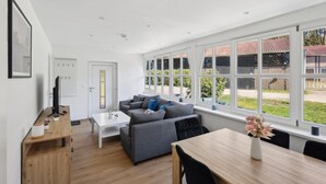 A modern living room with a sofa, a dining table, and large windows offering a view of the outside.