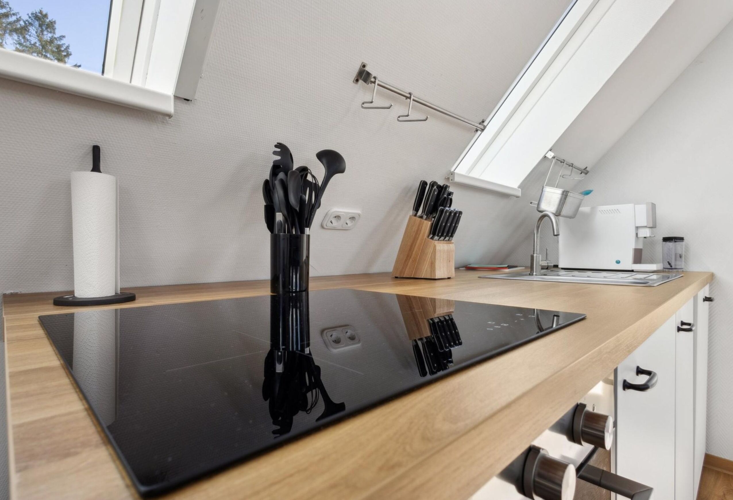 A modern kitchen with a black countertop, a coffee machine, and utensils hanging on the wall.