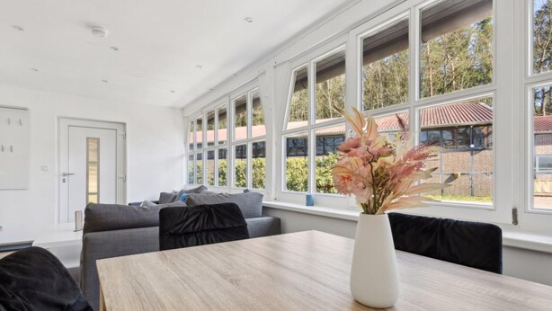 A modern room with a large window, a wooden table, and a vase of flowers.