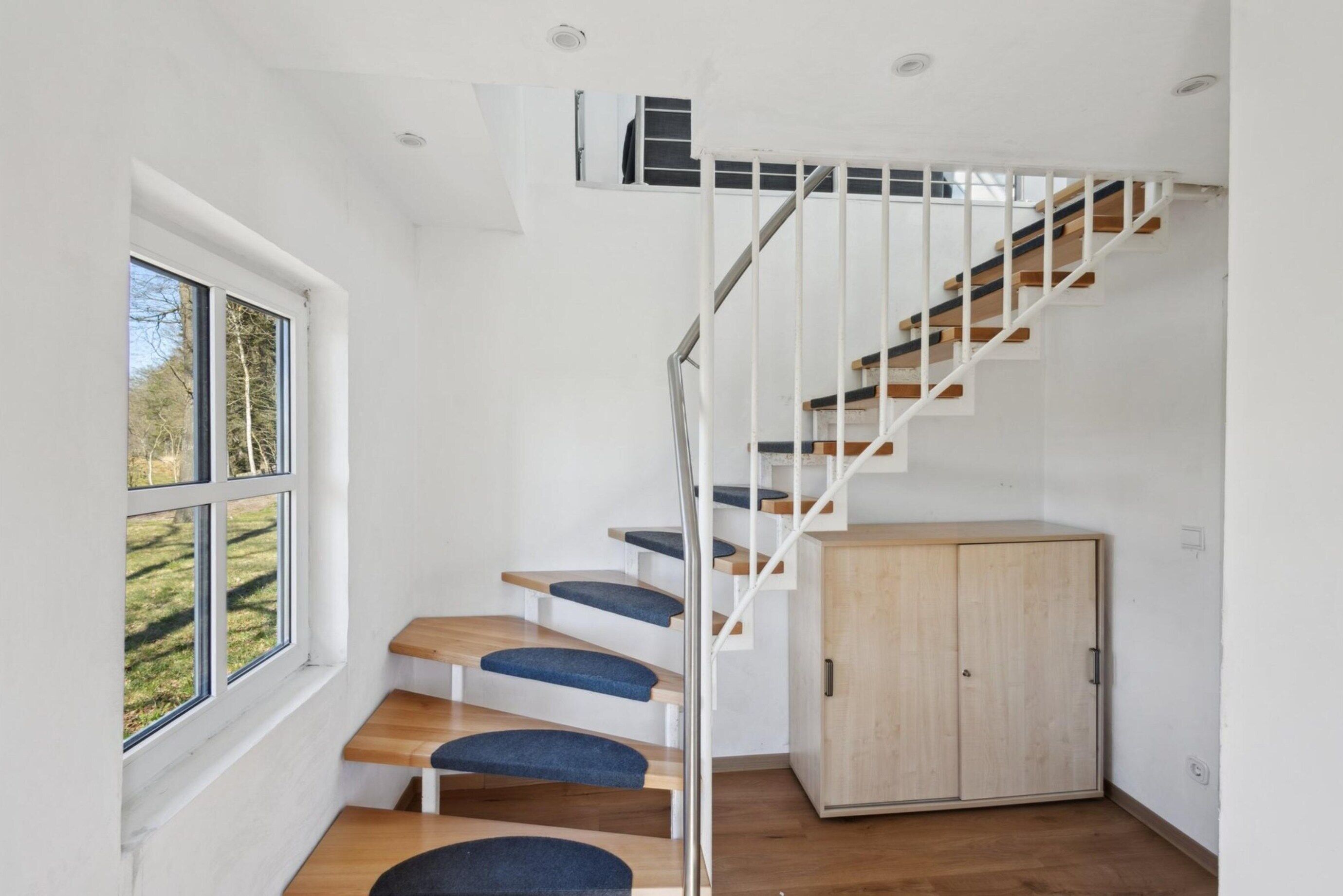 Una moderna scala con gradini in legno e pianerotti imbottiti blu, che conduce a una porta di legno in cima.