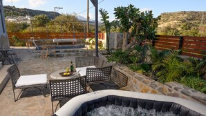 A hot tub with a stone patio, wicker chairs, and a table with drinks.