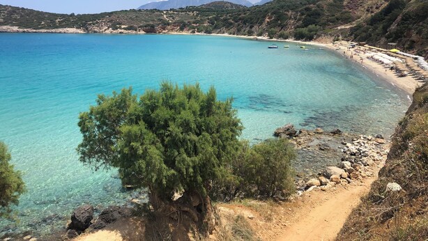 A coastal landscape with clear turquoise waters, a sandy beach, and rocky terrain.