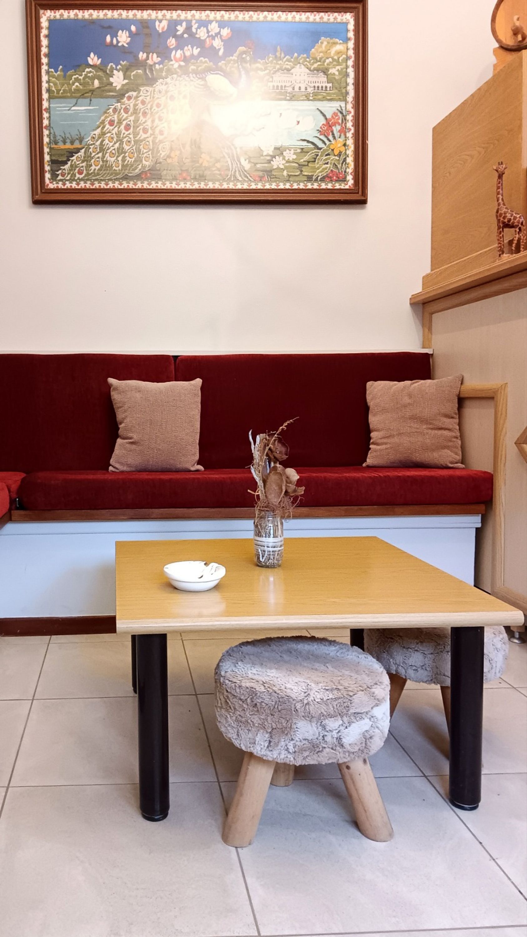 Et værelse med et træbord, en vase med tørre grene, en rød sofa med to puder, og et maleri over sofaen.