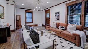 A spacious living room with a brown sofa, white armchair, and a coffee table. There is a wooden cabinet and a framed picture on the wall. - Downtown Tulsa’s Emerald on Carson (Tulsa)