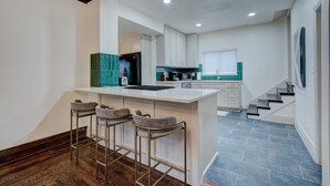 A modern kitchen with a central island, bar stools, and a staircase leading to another level. - Downtown Tulsa’s Emerald on Carson (Tulsa)