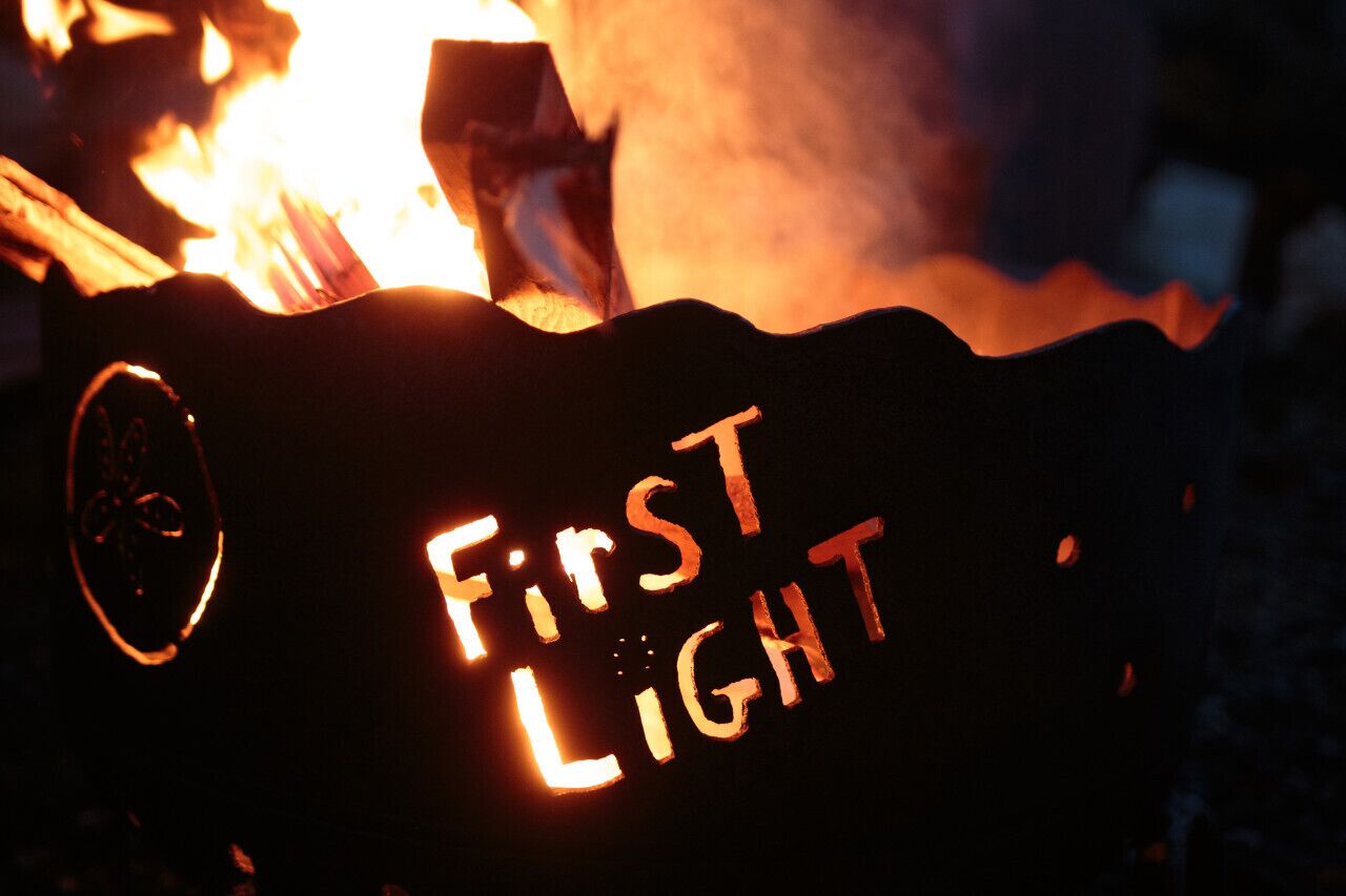 A sign with the words "First Light" illuminated by fire.