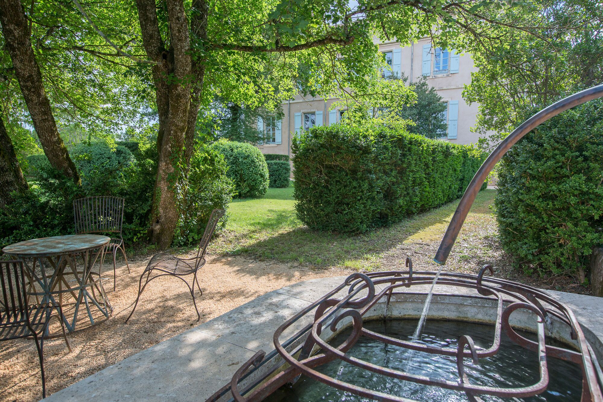 A garden with a metal bench, a small table, and a water feature.