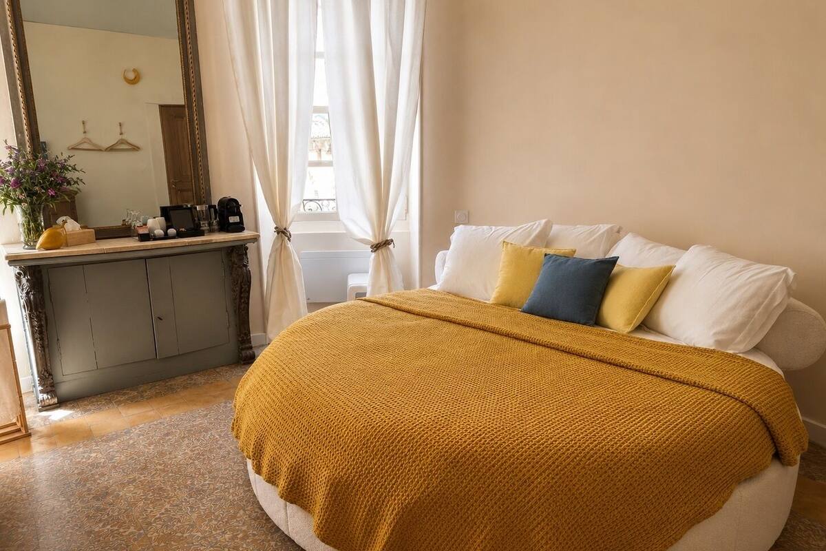 Un dormitorio con cama redonda, cómoda, espejo y ventana con cortinas.