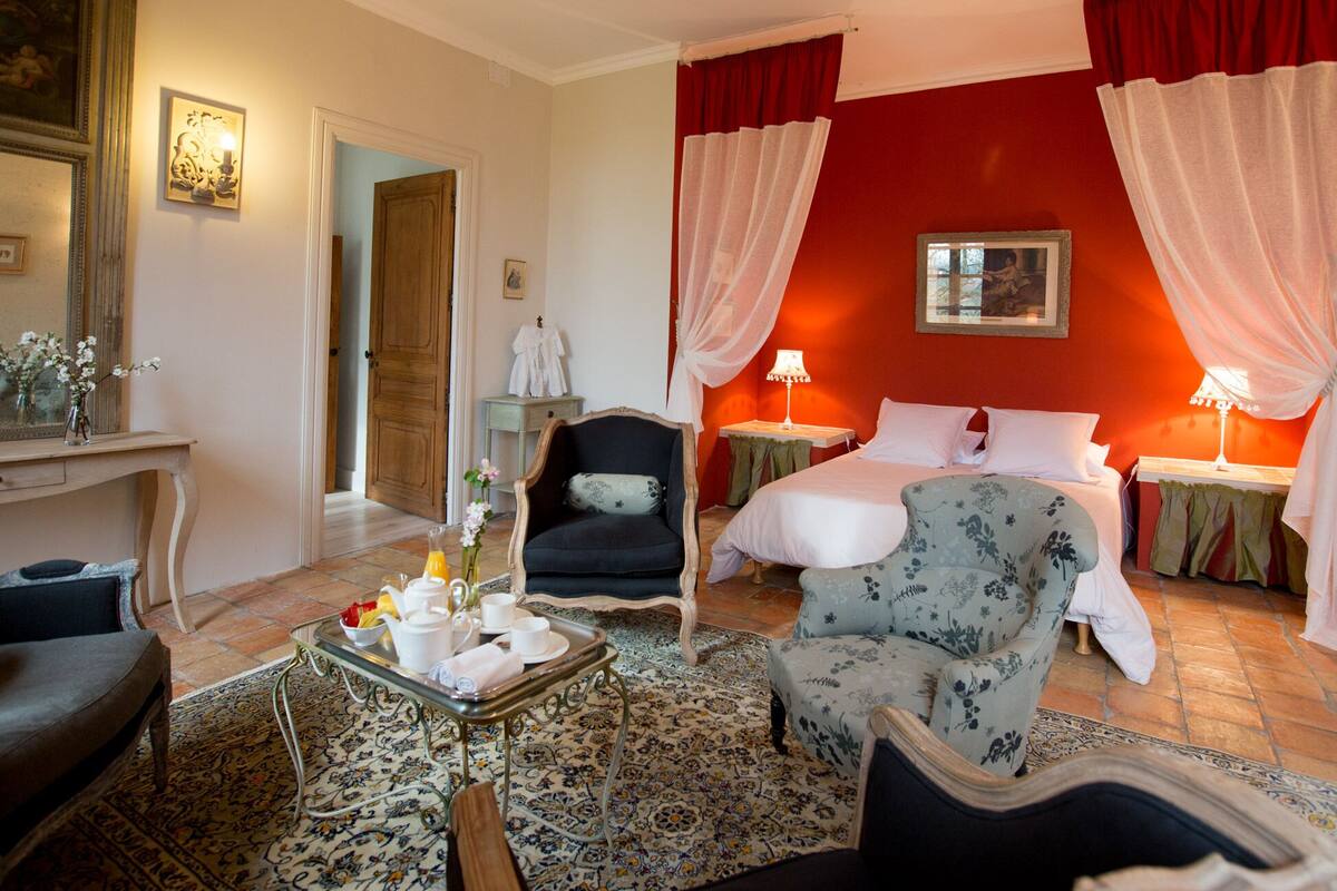 Una habitación de hotel con cama, dos mesitas de noche, una silla, una mesa con artículos de desayuno, un espejo y una puerta.