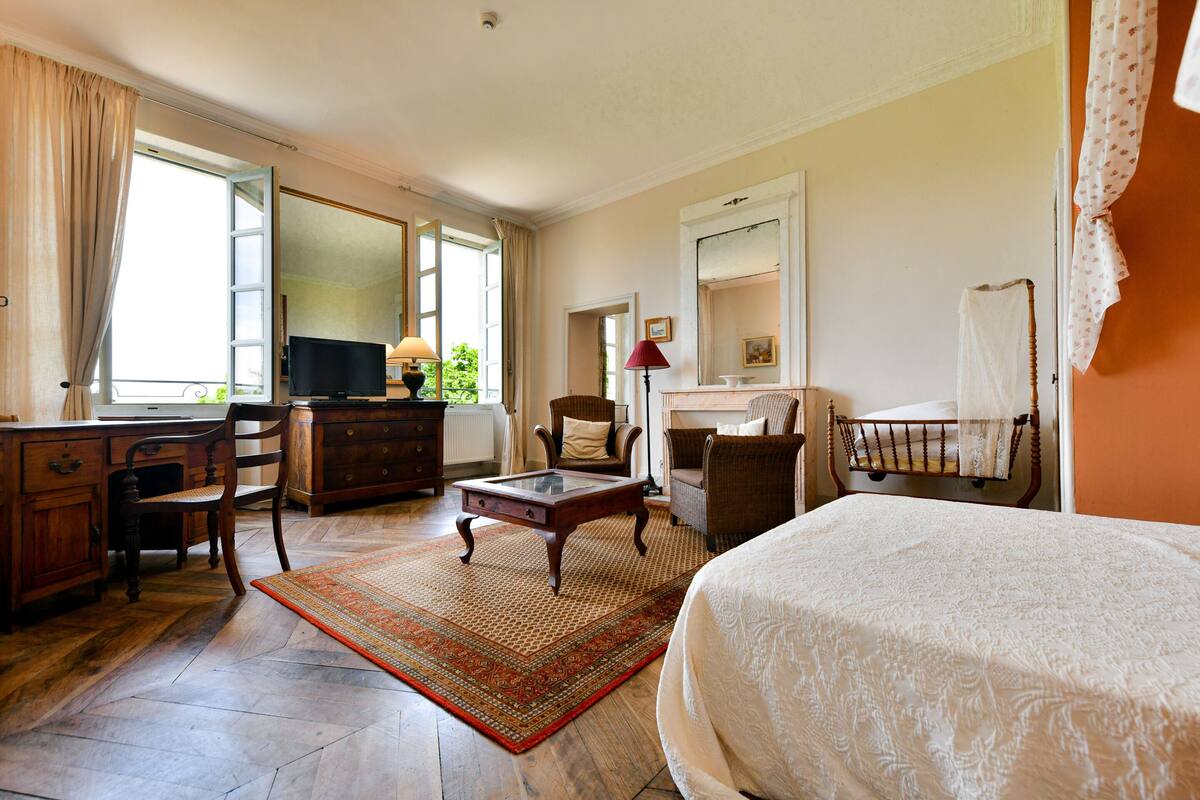 Habitación de hotel con cama, escritorio, televisor, silla, chimenea y ventana con cortinas.