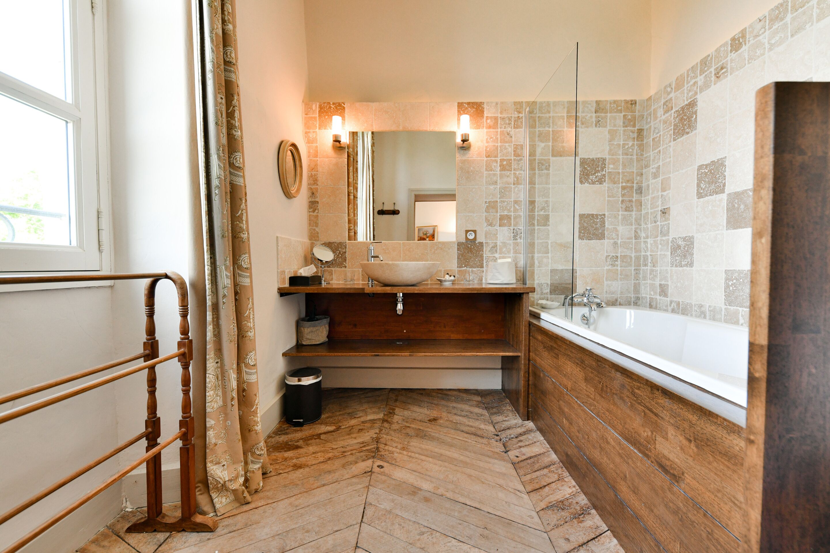 A bathroom with a wooden vanity, a large sink, a bathtub, and a herringbone-patterned floor.