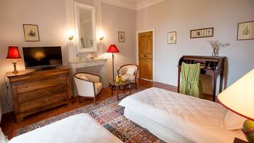 A hotel room with two beds, a desk with a television, a chair, a wooden wardrobe, and a desk lamp.