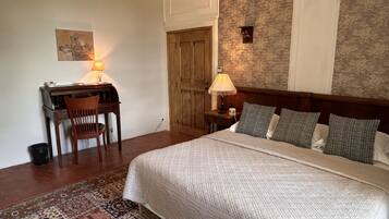 Una habitación de hotel con cama, escritorio, silla, lámparas y un tapete estampado.