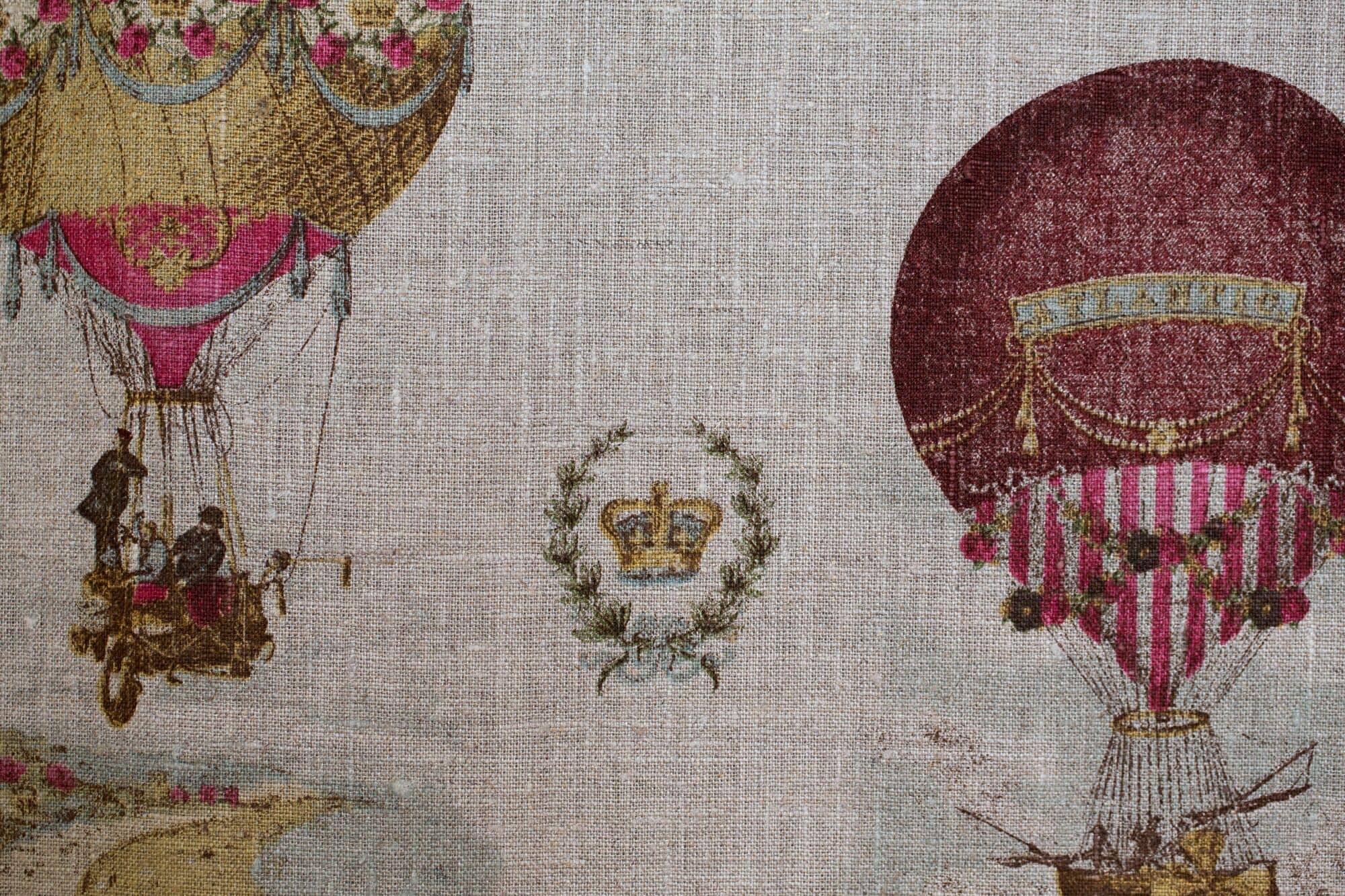 Stof met geborduurde motieven, waaronder een kroon, een luchtballon en een figuur op een schommel.