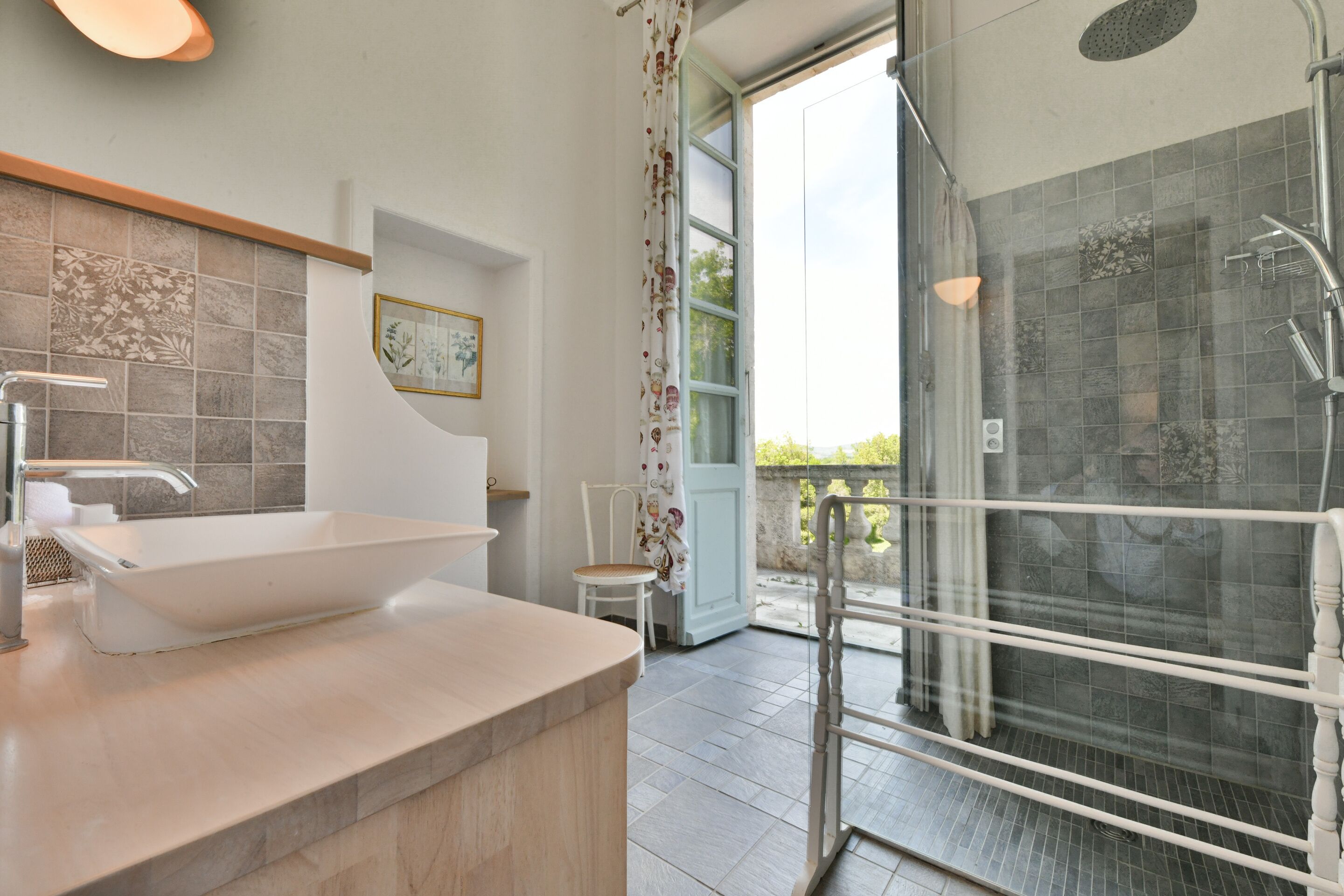 A modern bathroom with a large sink, shower, and a view of the outdoors.