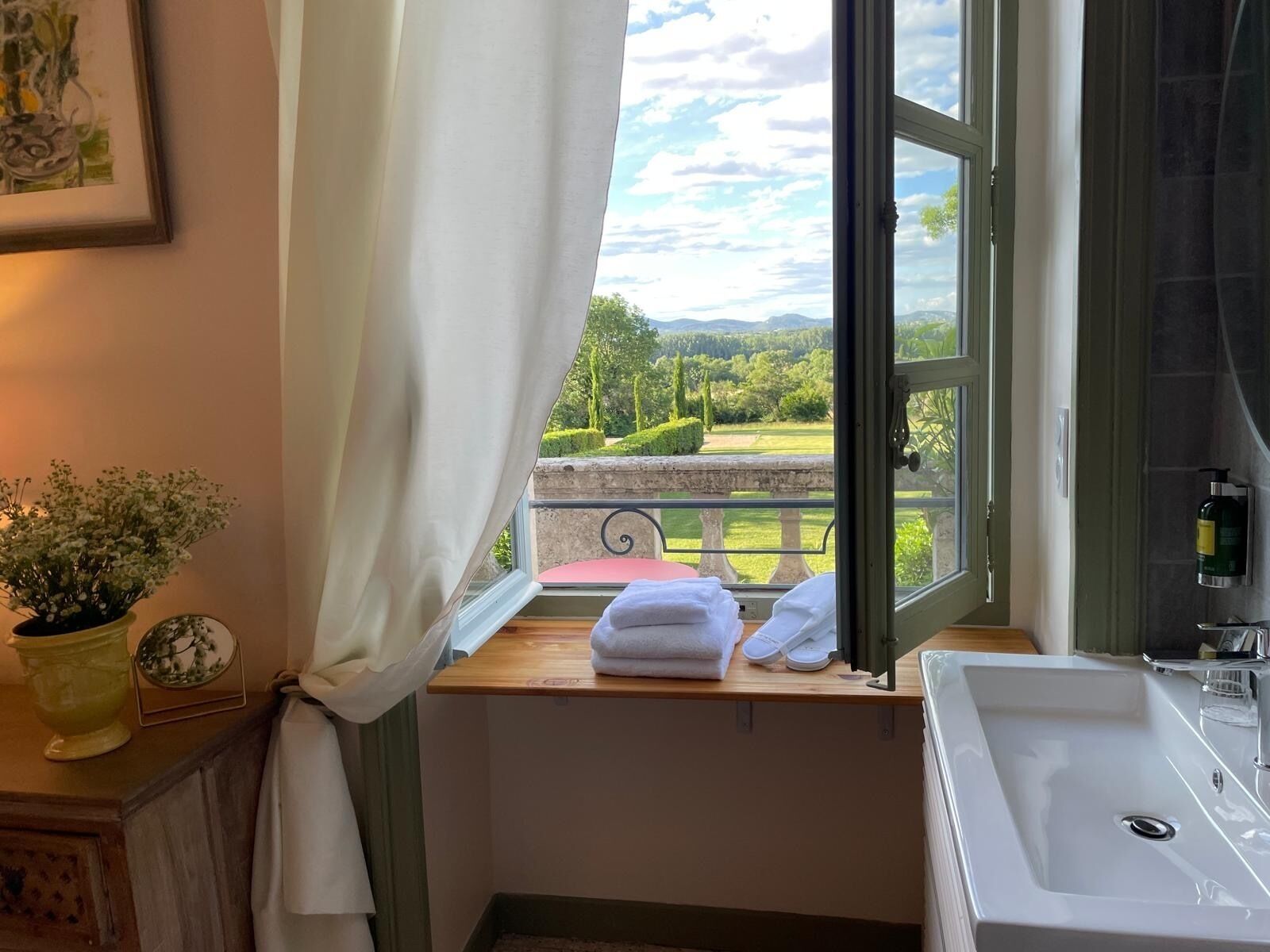 A bathroom with a large window, a sink, and a view of a green landscape.