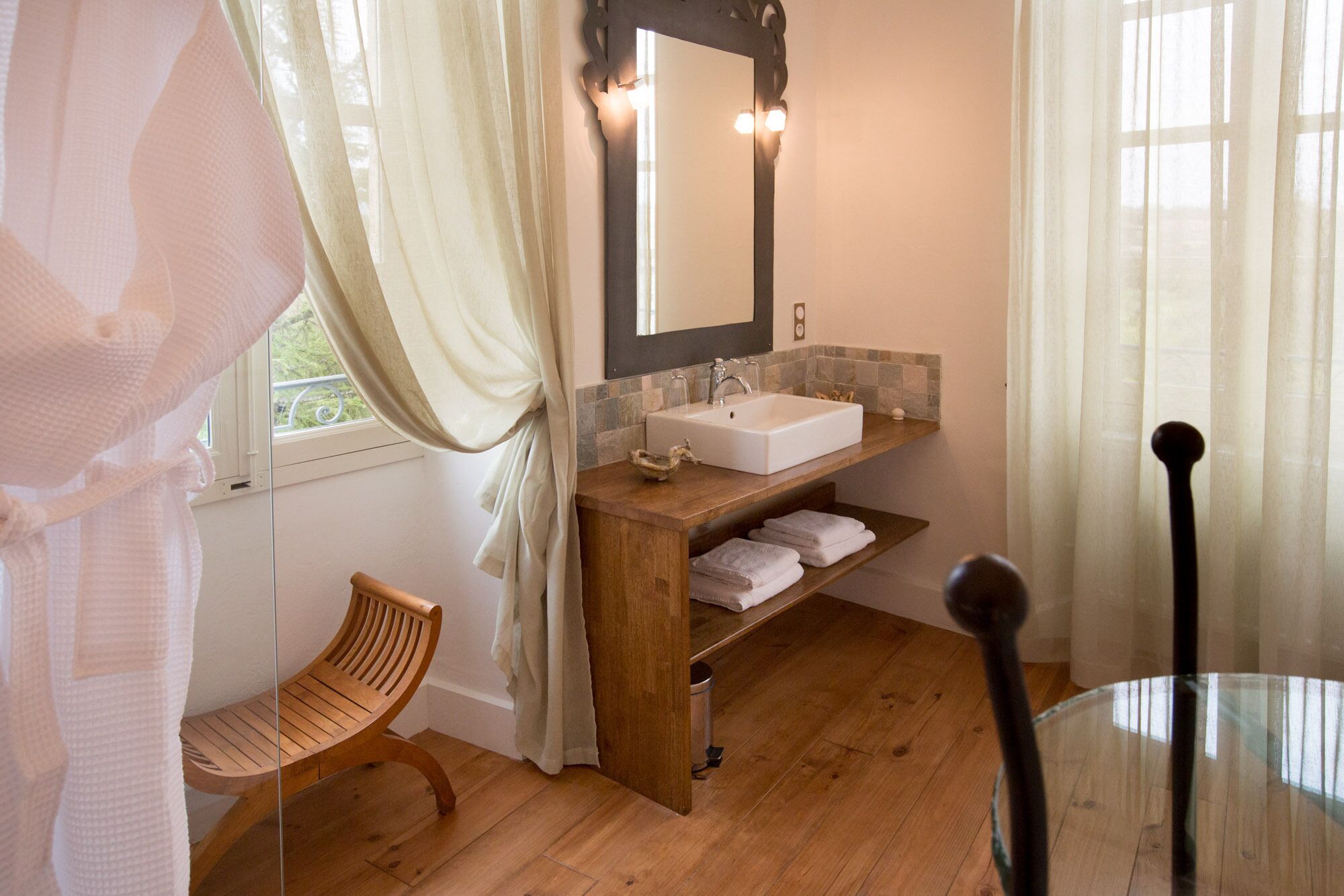 A bathroom with a wooden vanity, a white sink, a mirror, and a window with curtains.