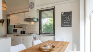 A modern kitchen with white cabinets, a wooden dining table, and a window with a view of greenery. - Holiday Home in Park De Watersnip Near Beach (Petten)