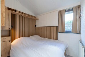 Camera da letto con testiera in listelli di legno, un letto singolo, una finestra con tende e un termosifone.