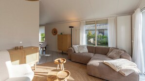 A modern living room with a sofa, a wooden cabinet, and a dining area with a table and chairs. - Holiday Home in Park De Watersnip Near Beach (Petten)