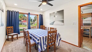 Ein Essbereich mit einem Tisch, der für sechs Personen gedeckt ist, Holzsesseln, einem Deckenventilator und Blick auf ein rotes Gebäude.