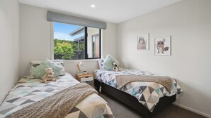 A bedroom with two beds, a window with a view of greenery, and two wall-mounted pictures. - Rangi Marie - Alexandra Holiday Home (Alexandra)
