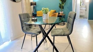 Een eetgedeelte met een glazen tafel, vier grijze stoelen, een potplant en een blauwe wand.