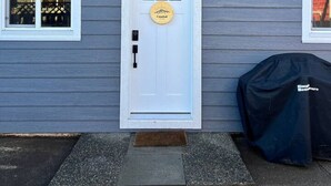 A house with a white front door, a small porch, and a covered grill to the right. - Coastal Suite – Waterfront Harbour Retreat in the Heart of Ucluelet (Ucluelet)
