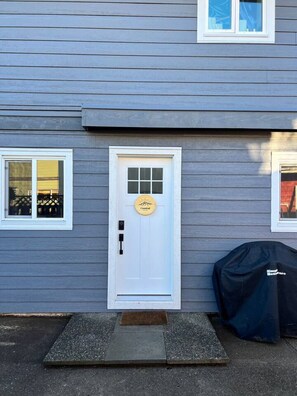 A house with a white front door, a small porch, and a covered grill to the right. - Coastal Suite – Waterfront Harbour Retreat in the Heart of Ucluelet (Ucluelet)