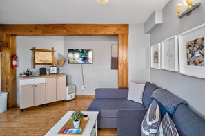 A modern living space with a wooden ceiling, a grey sofa, a white coffee table with a plant, and a kitchen area with a map and a TV.